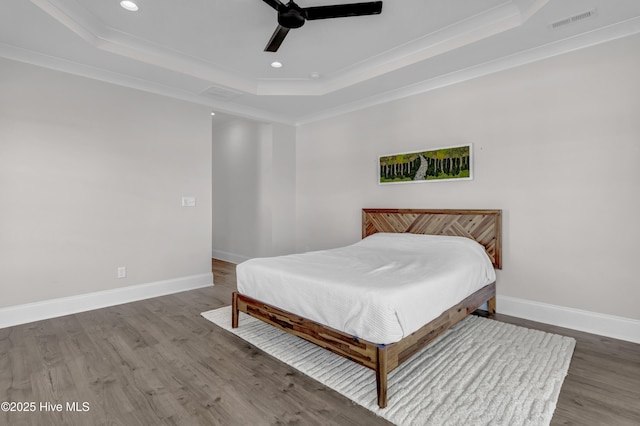 bedroom with a tray ceiling, crown molding, wood finished floors, and baseboards