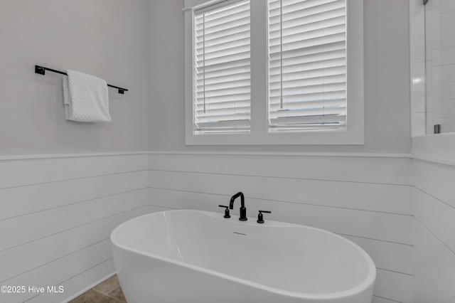 bathroom with plenty of natural light, a soaking tub, and wainscoting