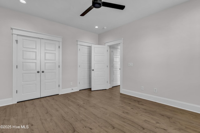 unfurnished bedroom with recessed lighting, baseboards, multiple closets, and wood finished floors