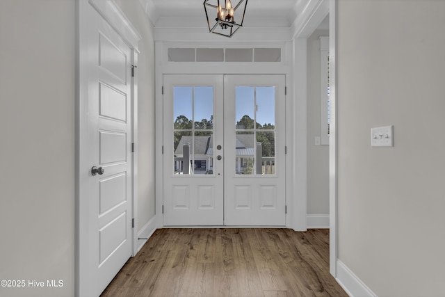 doorway to outside with ornamental molding, wood finished floors, french doors, an inviting chandelier, and baseboards