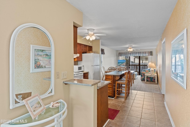 kitchen featuring white appliances, light tile patterned floors, brown cabinetry, baseboards, and a peninsula