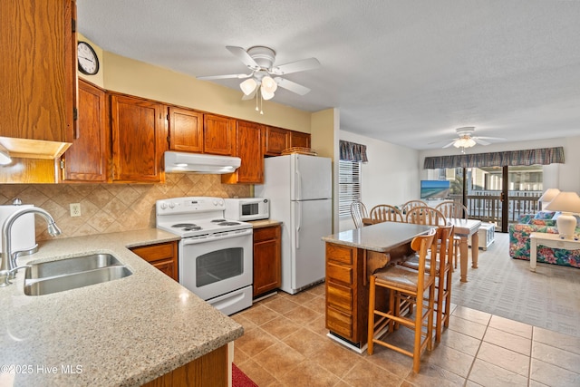 kitchen featuring a sink, under cabinet range hood, white appliances, brown cabinetry, and decorative backsplash