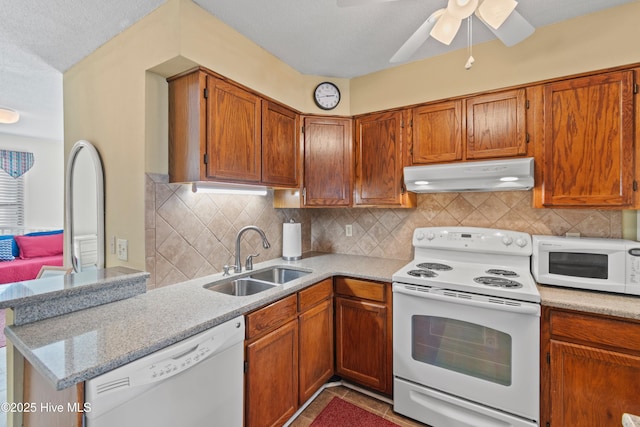 kitchen with white appliances, a sink, decorative backsplash, under cabinet range hood, and brown cabinets