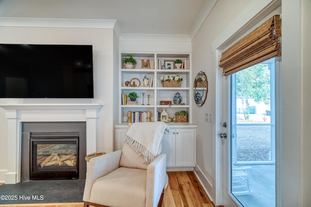 sitting room with a glass covered fireplace, crown molding, and light wood finished floors