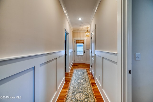 corridor featuring crown molding, a decorative wall, wood finished floors, and a wainscoted wall