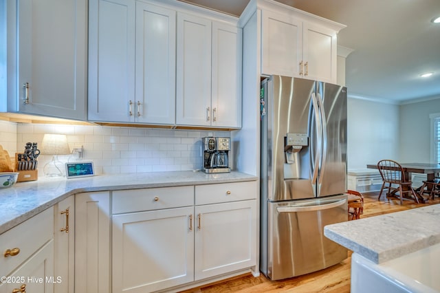 kitchen featuring tasteful backsplash, crown molding, light stone countertops, stainless steel fridge, and white cabinetry