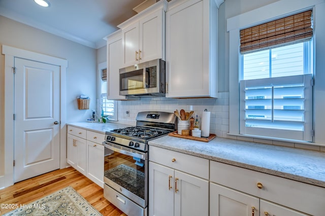 kitchen with light wood-type flooring, stainless steel appliances, white cabinets, crown molding, and decorative backsplash