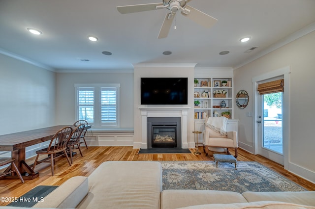 living room featuring a fireplace with flush hearth, plenty of natural light, wood finished floors, and crown molding