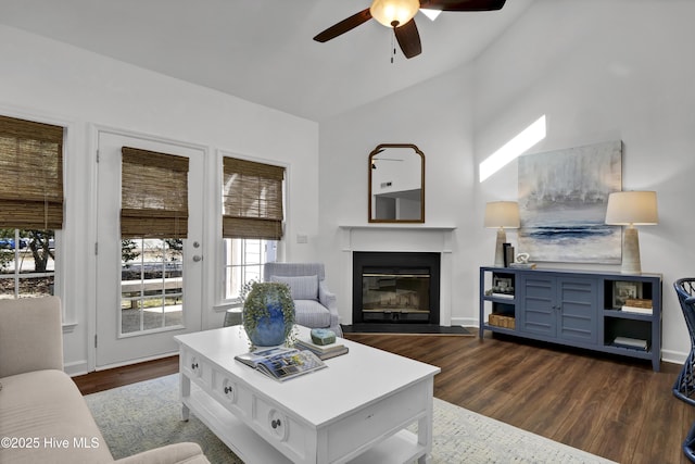 living area with a glass covered fireplace, dark wood finished floors, baseboards, and ceiling fan