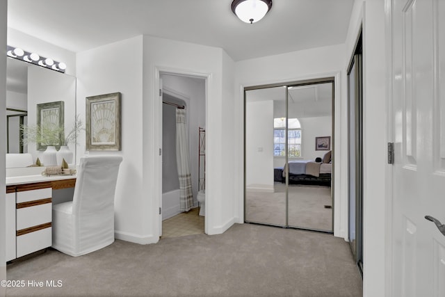 bedroom featuring a closet, baseboards, light colored carpet, and ensuite bath