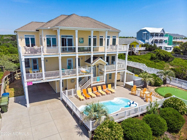 rear view of property with a balcony, fence, a fenced in pool, driveway, and a patio area