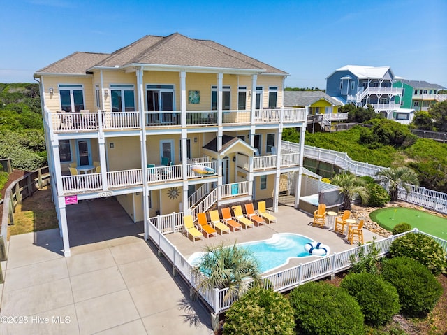 rear view of house featuring a fenced in pool, fence, roof with shingles, a balcony, and a patio area