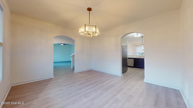 unfurnished room with light wood-type flooring, ceiling fan with notable chandelier, a sink, arched walkways, and baseboards