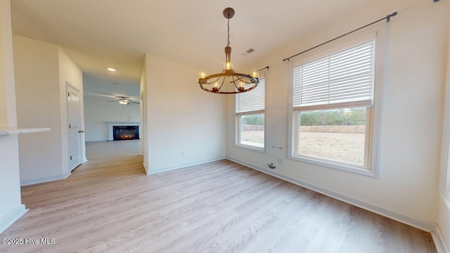 unfurnished room featuring light wood-style floors, baseboards, a warm lit fireplace, and a chandelier