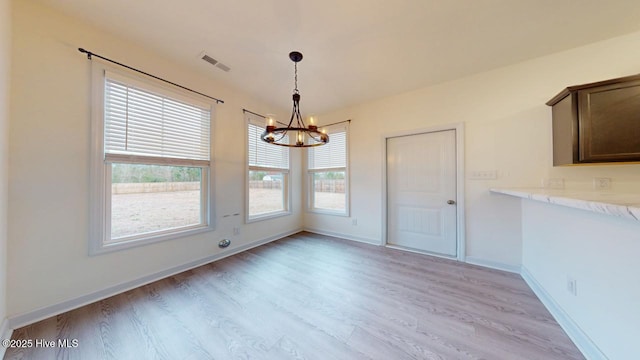 unfurnished dining area with visible vents, light wood-style flooring, baseboards, and an inviting chandelier