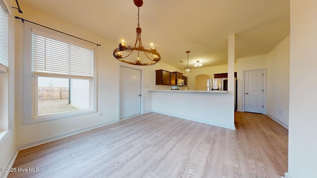 unfurnished living room featuring a chandelier, light wood finished floors, baseboards, and arched walkways