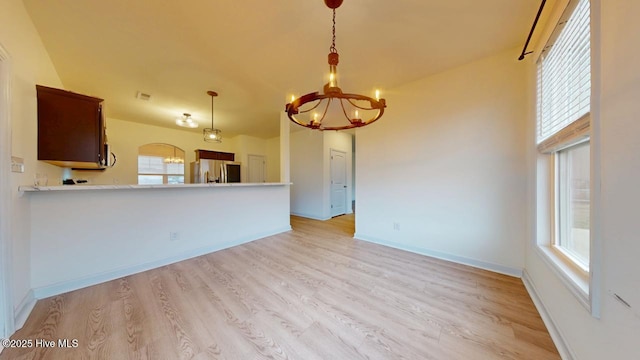 unfurnished living room featuring visible vents, baseboards, a chandelier, light wood-style flooring, and arched walkways