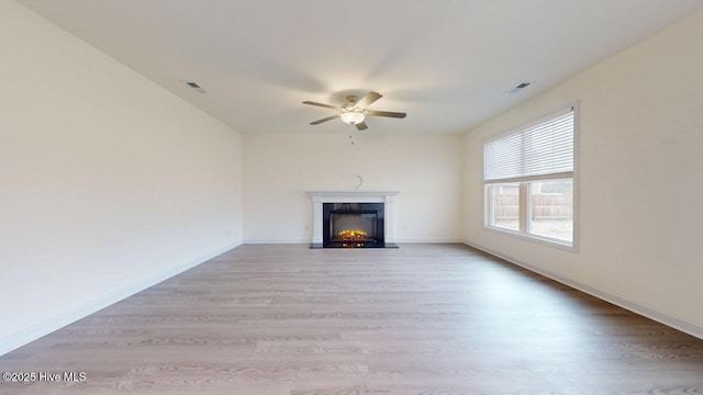 unfurnished living room featuring visible vents, a warm lit fireplace, light wood-style flooring, and a ceiling fan