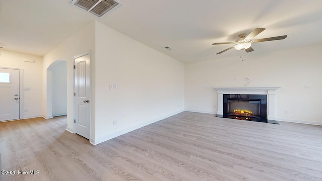 unfurnished living room with visible vents, baseboards, light wood-type flooring, a lit fireplace, and a ceiling fan