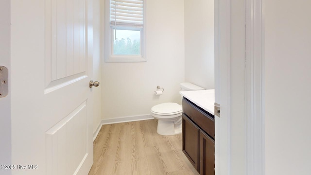 half bathroom with vanity, toilet, wood finished floors, and baseboards