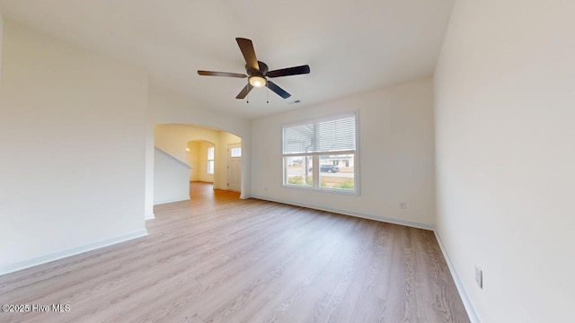 spare room featuring arched walkways, light wood finished floors, baseboards, and ceiling fan