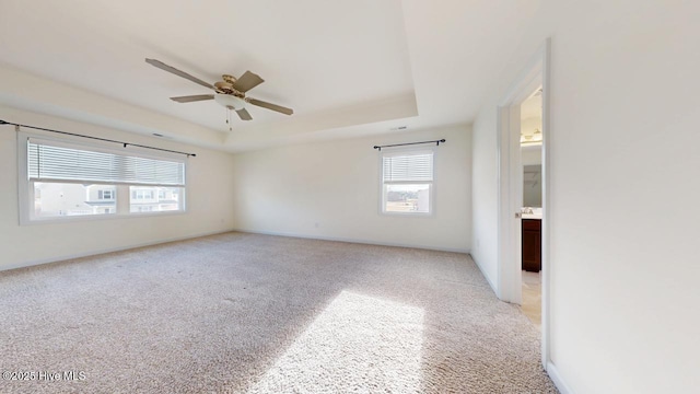 empty room featuring a tray ceiling, a ceiling fan, baseboards, and light carpet