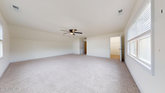 empty room with a ceiling fan, vaulted ceiling, light colored carpet, and visible vents