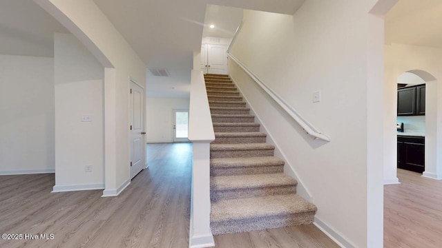 stairs featuring visible vents, baseboards, arched walkways, and wood finished floors