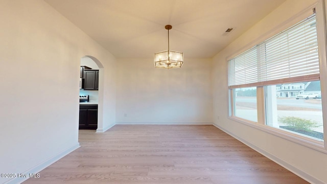 empty room with visible vents, baseboards, light wood-style flooring, arched walkways, and a notable chandelier