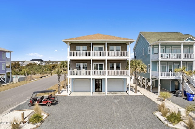 449 E Fourth St, Ocean Isle Beach, NC 28469 - coastal inspired home featuring gravel driveway, an attached garage, a balcony, and a shingled roof