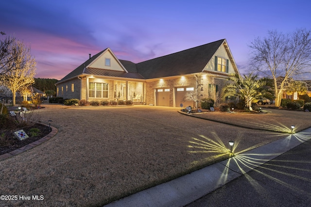 view of front of home featuring brick siding, an attached garage, metal roof, driveway, and a standing seam roof