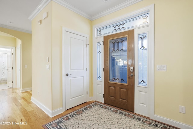 entrance foyer featuring baseboards, arched walkways, ornamental molding, and light wood finished floors