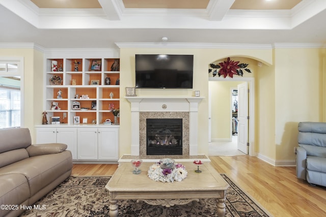 living room featuring baseboards, ornamental molding, beam ceiling, a fireplace, and light wood-style floors