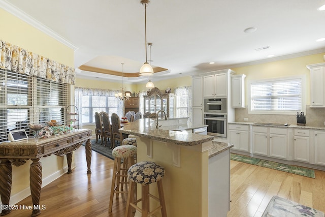 kitchen with double oven, a kitchen bar, light wood-type flooring, ornamental molding, and a sink