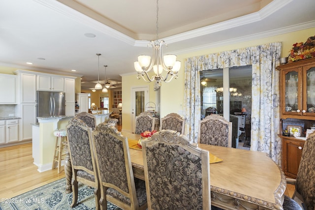 dining room featuring a raised ceiling, ceiling fan with notable chandelier, light wood finished floors, and ornamental molding