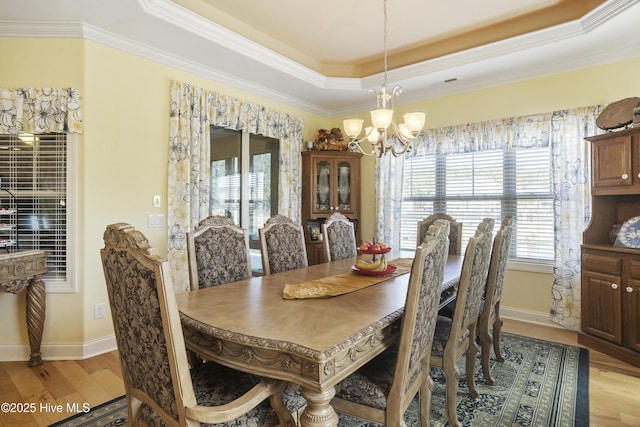 dining room featuring a raised ceiling, light wood-style floors, baseboards, and a chandelier