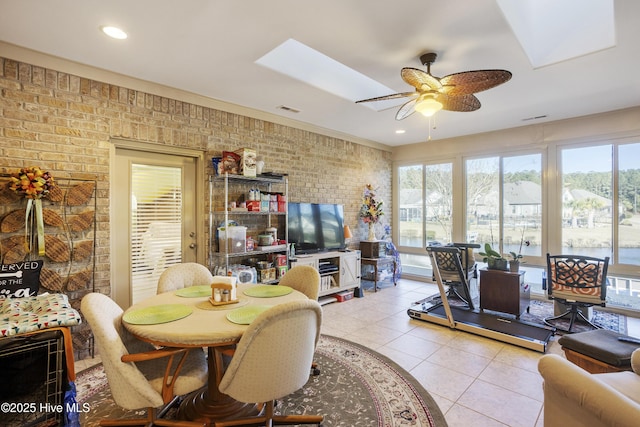 dining area featuring visible vents, brick wall, a skylight, light tile patterned flooring, and ceiling fan