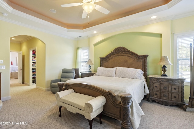 carpeted bedroom with a spacious closet, baseboards, ornamental molding, arched walkways, and a raised ceiling