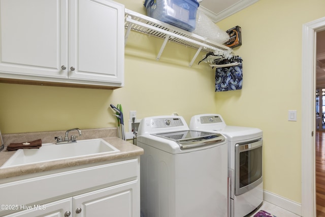 laundry area with baseboards, separate washer and dryer, cabinet space, a sink, and crown molding