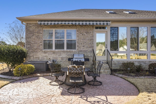 rear view of property with brick siding, a patio, and roof with shingles