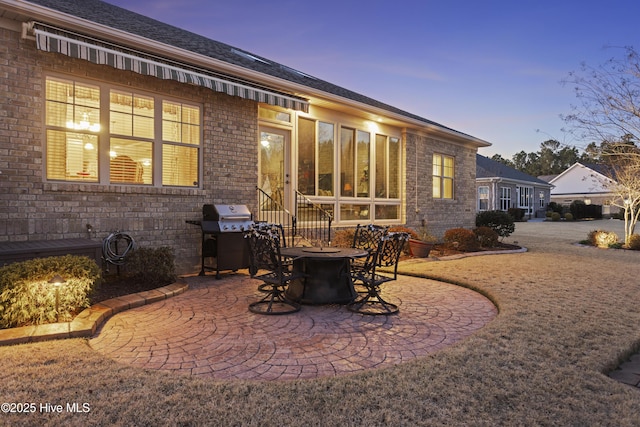 back of property at dusk featuring a patio area and brick siding