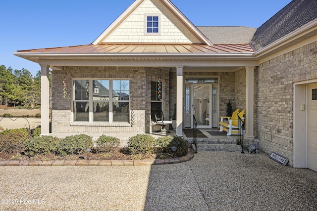 doorway to property featuring metal roof, brick siding, a porch, and a standing seam roof