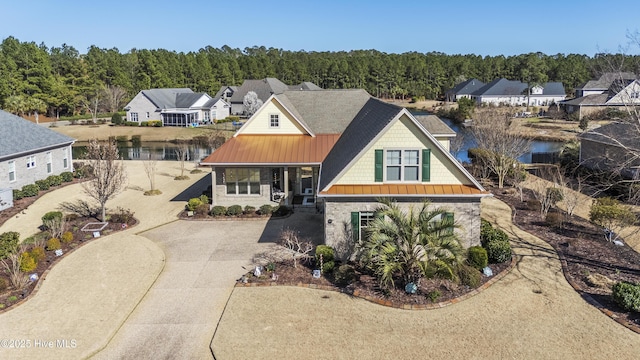 view of front of house with a water view, metal roof, stone siding, driveway, and a standing seam roof