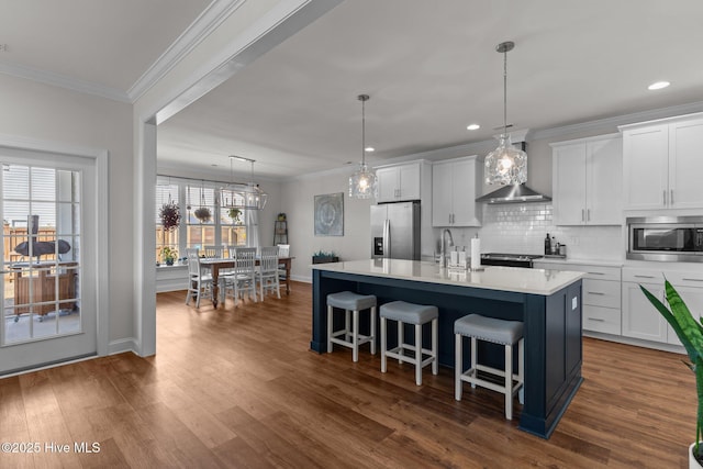 kitchen with a kitchen island with sink, appliances with stainless steel finishes, wall chimney exhaust hood, and ornamental molding