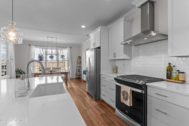 kitchen featuring wood finished floors, a sink, light countertops, appliances with stainless steel finishes, and wall chimney exhaust hood