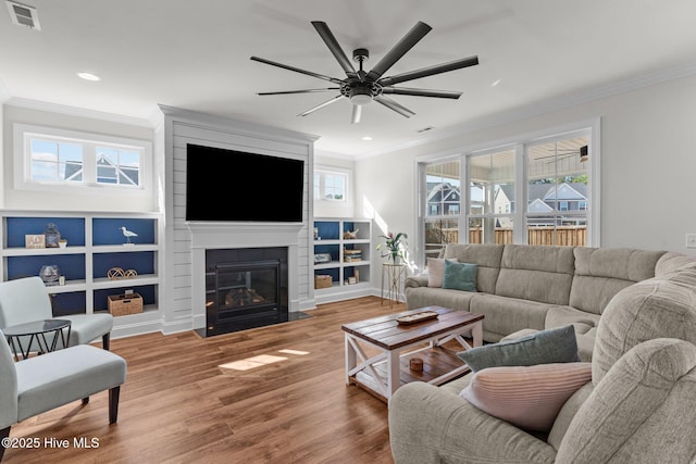 living room featuring visible vents, a large fireplace, ornamental molding, wood finished floors, and a ceiling fan