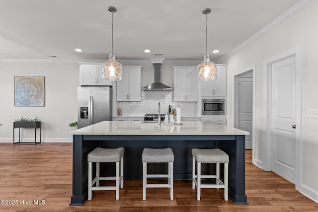 kitchen with a center island with sink, stainless steel appliances, wall chimney exhaust hood, and white cabinetry