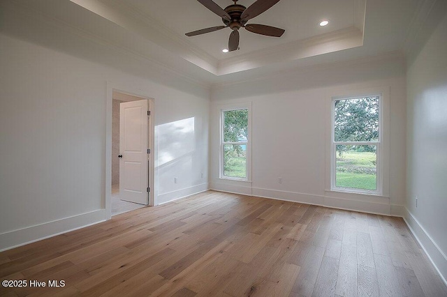 unfurnished room with light wood-type flooring, a raised ceiling, and ornamental molding