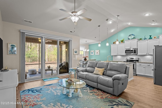 living room with a wealth of natural light, visible vents, ceiling fan with notable chandelier, and light wood finished floors