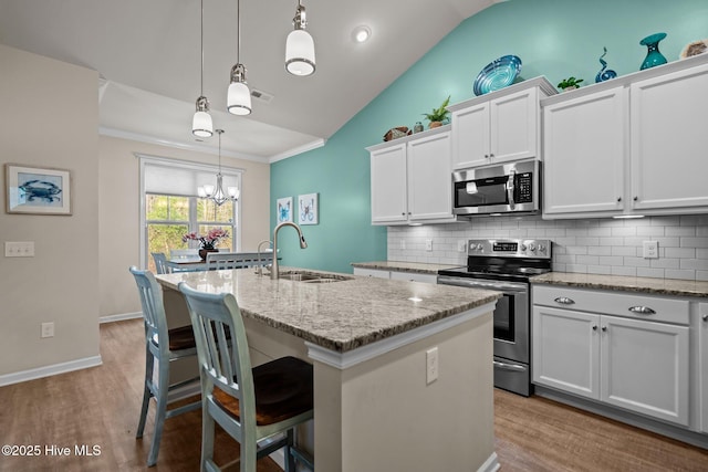 kitchen with an island with sink, a sink, stainless steel appliances, vaulted ceiling, and backsplash